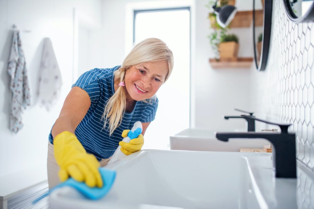 Senior woman with gloves cleaning bathroom indoors at home